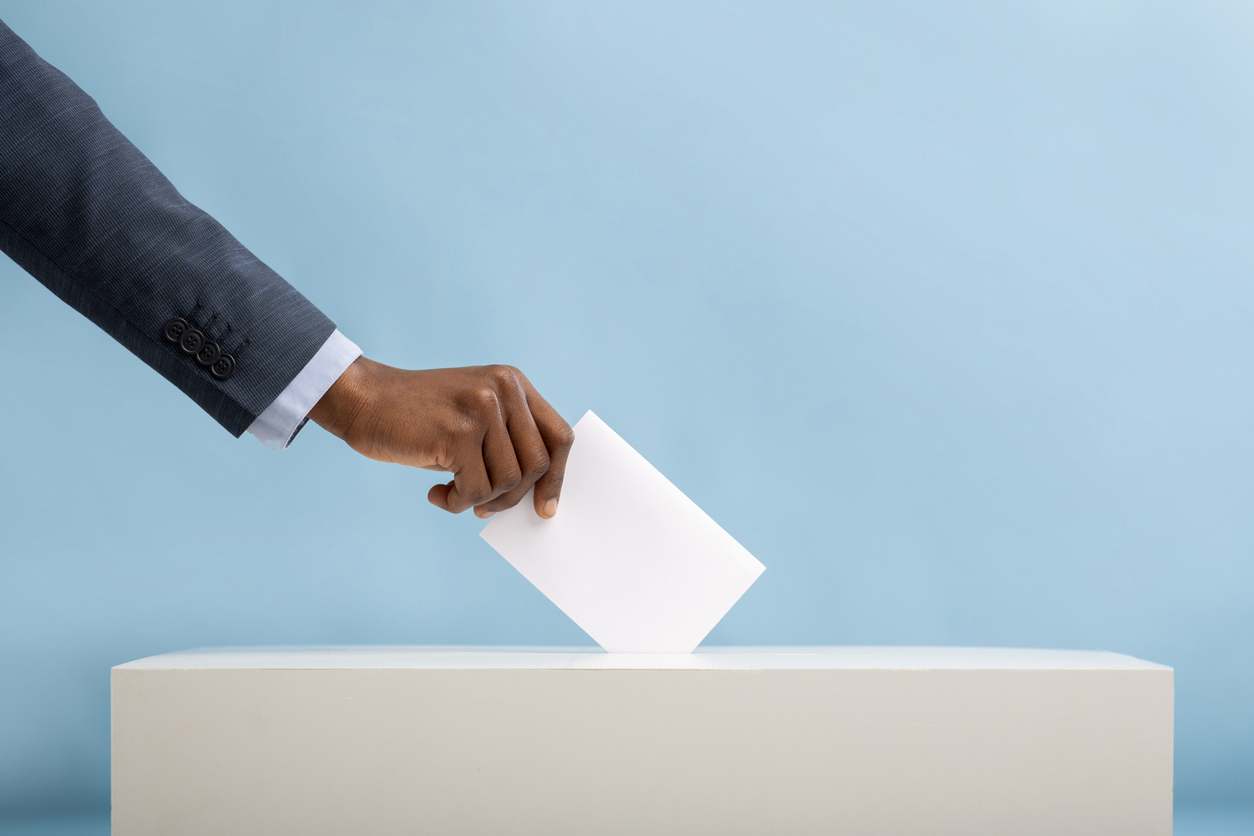 Person in suit sticking vote into polling box with blue background