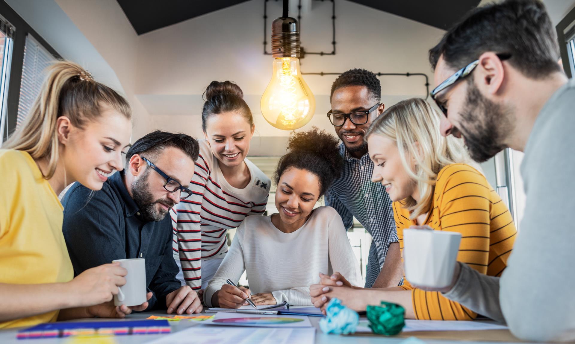 Seven people around table with lightbulb and notebook