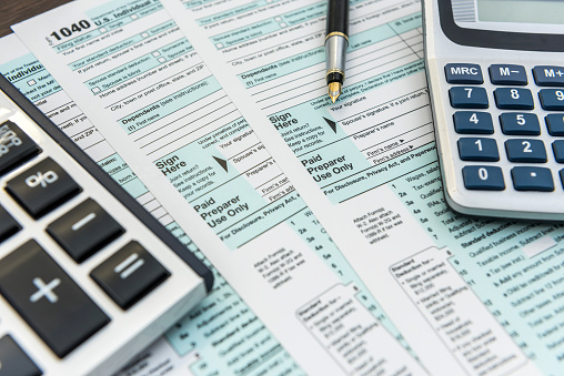 1040 Tax forms, two calculators and a fountain pen lying on a table