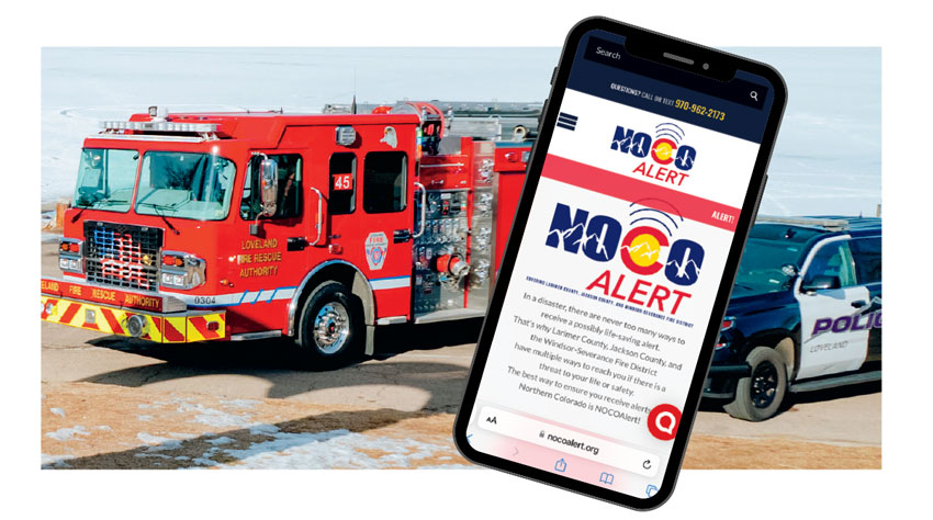 A cell phone with the NOCO Alert website on display superimposed over a photo of a fire truck and police car.